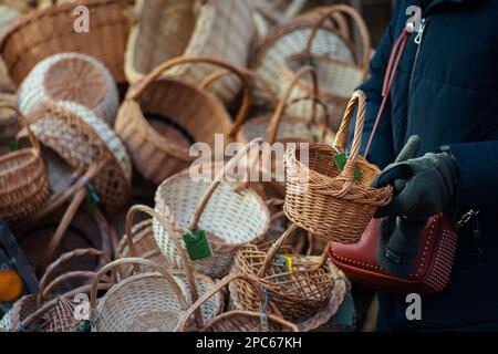 Gruppe leerer Korbkörbe zum Verkauf auf einem Straßenmarkt oder einem traditionellen Jahrmarkt mit einer Frau, die einen Korb auswählt Stockfoto