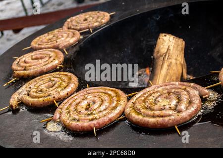 In der Nähe befinden sich Spiralwürstchen, die zum Essen zubereitet, gegrillt oder geröstet werden, an einem offenen Feuer, auf einem Lebensmittelmarkt oder bei einem Picknick im Freien Stockfoto