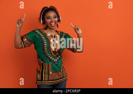 Lustige afrikanische Frau in Nationalkostüm, die Spaß auf Orange hat Stockfoto