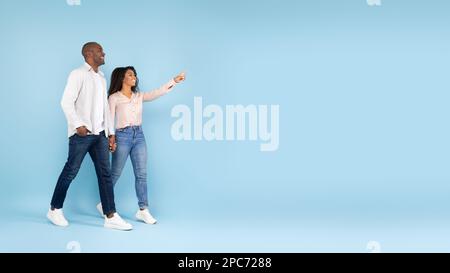 Aufgeregte afroamerikanische Ehepartner, die Händchen halten und laufen, zeigen und schauen sich Werbetexte an, Banner Stockfoto
