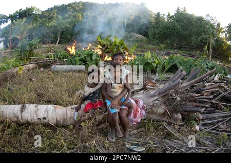 Familie sitzt auf einem Baum in der Nähe von brennendem Müll, Warmindi, Bird's Head Halbinsel, Raja Ampat Inseln (vier Könige), West Papua, Neuguinea Stockfoto