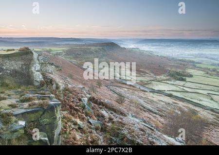 Blick auf Klippen und Moorland über das Tal bei Sonnenaufgang, Blick von Curbar Edge in Richtung Baslow Edge, Dark Peak, Peak District N. P. Derbyshire Stockfoto