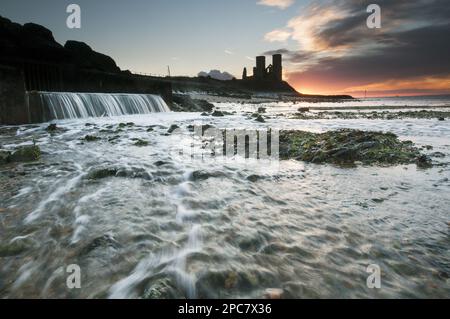 Blick auf den Strand und den Ausgang, mit einer zerstörten Kirche aus dem 12. Jahrhundert in der Ferne, Silhouette bei Sonnenaufgang, St. Mary's Church, Reculver, Kent, England, Vereinigt Euch Stockfoto