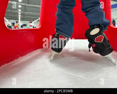 Einsteiger-Schlittschuhläufer mit einem Plastikläufer zur Unterstützung. Stockfoto