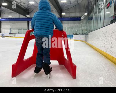 Einsteiger-Schlittschuhläufer mit einem Plastikläufer zur Unterstützung. Stockfoto