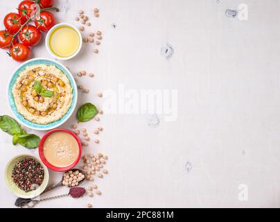 Schüssel mit Hummus, Kichererbse, Tahini, Olivenöl, Sesamsamen, Kirschtomaten und Kräuter auf weißem rustikalem Holzhintergrund. Platz für Text. Lebensmittelgestell. Stockfoto