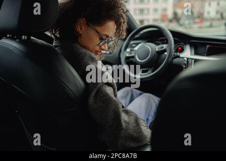 Eine junge Frau mit Brille schnallt sich vor dem Anlassen des Autos an. Sicherheitskonzept Fahren Stockfoto