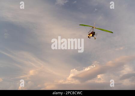 Das Propellerflugzeug fliegt am Sonnenuntergang. Ein kleiner privater Drachenflieger in einem bewölkten Himmel. Stockfoto