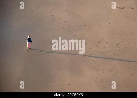 Nicht erkannte Person, die bei Sonnenuntergang am Sandstrand spaziert. Gesunder Lebensstil. Sport im Freien Stockfoto