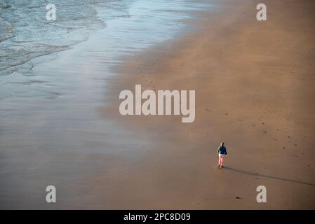 Nicht erkannte Person, die bei Sonnenuntergang am Sandstrand spaziert. Gesunder Lebensstil. Sport im Freien Stockfoto