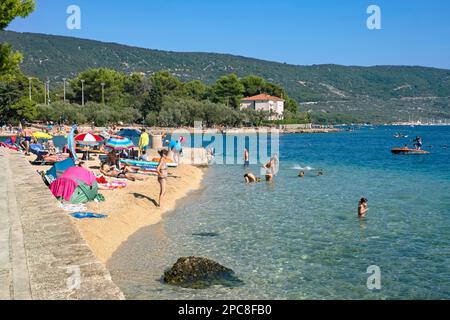 Sonnenanbeter am Sandstrand und Touristen, die in der Adria in der Nähe von Cres auf der Insel Cherso, Kvarner Bay, Primorje-Gorski Kotar, Kroatien schwimmen Stockfoto