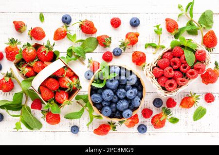 Verschiedene frische Beeren im Korb auf weißem Holzhintergrund, Draufsicht. Konzept der Sommerkost. Flach liegend, Kopierplatz. Stockfoto