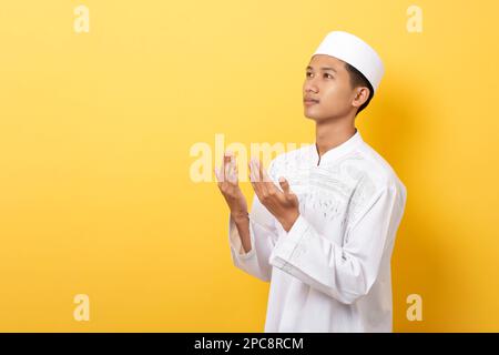 Junger, attraktiver asiatischer religiöser moslem betet isoliert auf orangefarbenem Hintergrund Stockfoto