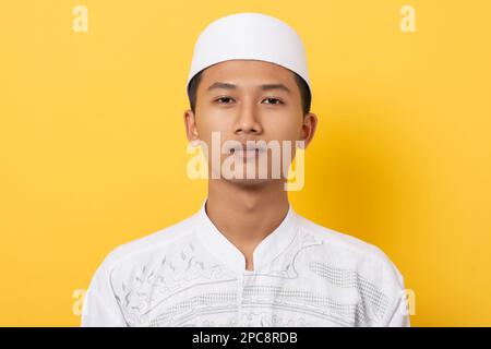 Junger, gutaussehender asiatischer moslem, der während des ramadan auf orangefarbenem Hintergrund Grußworte schickt. Fröhlicher ramadan und eid al fitr. Stockfoto