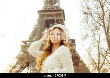 Ein unglaublich schönes Mädchen in einem langen weißen Kleid und einer Baskenmütze vor dem Hintergrund des Eiffelturms. Mode in Paris, Reisen und Hochzeiten. Rom Stockfoto