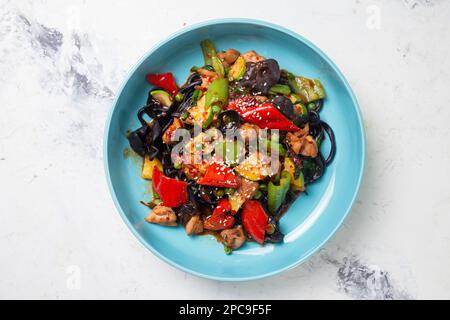 Draufsicht auf den schwarzen Lagman mit Huhn und Pfeffer auf einem blauen Teller. Stockfoto