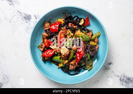 Draufsicht auf den schwarzen Lagman mit Huhn und Pfeffer auf einem blauen Teller. Stockfoto