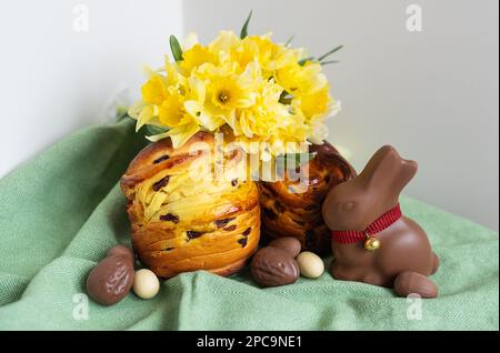 Hausgemachtes traditionelles Ostergebäck liegt auf einer grünen Serviette zusammen mit Narzissen, Kaninchen und Schokoladeneiern. Osterbacken und Dekoration Stockfoto