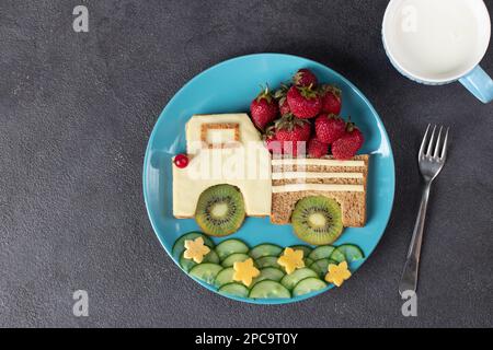 Gesunder Toast für Kinder in Form eines Autos mit Erdbeeren, Kiwi und Käse auf blauem Teller, Draufsicht Stockfoto