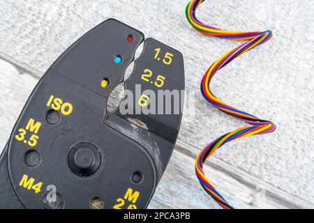 Nahaufnahme des in China hergestellten Abisolierers und Drahtschneiders ohne Markenkennzeichnung für 26-10AWG-Draht (siehe Hinweise) mit Spulen aus feinem, mehrfarbigem Elektrodraht. Stockfoto