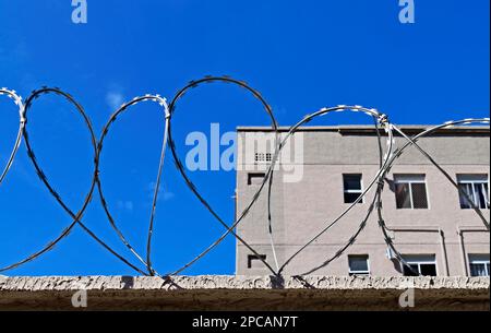 Stacheldraht an der Oberseite der Wand und graue Buikings im Hintergrund Stockfoto