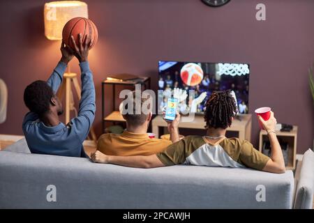 Rückblick auf eine Gruppe von Freunden, die zu Hause ein Basketballspiel anschauen und Bier trinken Stockfoto