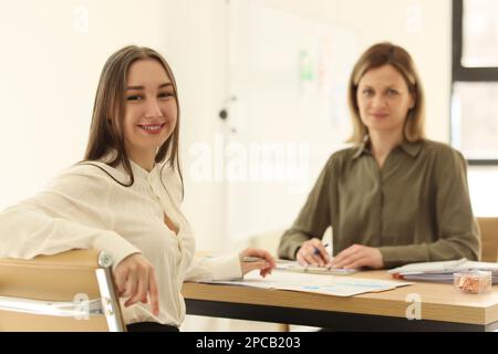 Zwei lächelnde Frauen sitzen am Bürotisch und schauen in die Kamera. Stockfoto