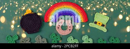 St. Patrick's Day Konzept. Gestrickte Komposition aus grünem Hut, goldenem Topf, Hufeisen, Regenbogen und grünen Shamrocks auf grünem Hintergrund mit Magazin Stockfoto