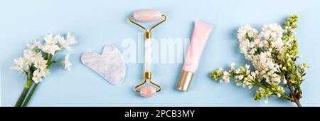 Rosa Jade Roller und Gua Sha für Gesichtsmassage mit Creme oder Gel für das Gesicht und Blumen Narzissen und Flieder. Massagegeräte für das Gesicht. Anti-Alter, Liftin Stockfoto