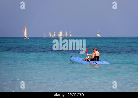 Kajakfahren auf dem Meer, Mann mit Schwimmweste rudert mit einem Ruder im Kanu auf Segelbooten im Hintergrund. Reise- und Wassersportkonzept Stockfoto