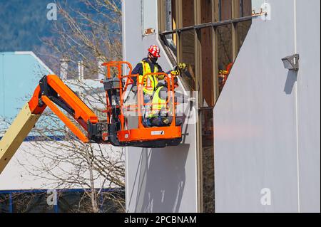 Zwei Männer in Warnwesten und Schutzhelmen auf einem Aufzug, die Fenster in einem Geschäftsgebäude installieren. Port Coquitlam, B.C., Kanada. Stockfoto