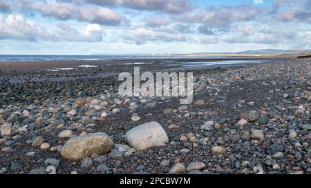 Wellen schlagen auf einen steinigen Strand vor Bootle in Cumbria an der Küste der Irischen See und blicken auf die Kernkraftanlage Sellafield, Cumbria