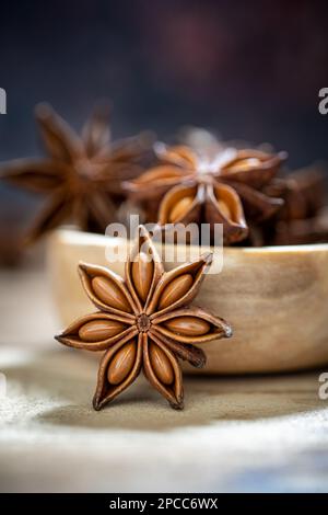 Anissterne (Illicium verum) in Holzschale auf dunklem rustikalem Holzhintergrund. Lieblingsspice in vielen Lebensmitteln und für die Medizin. Duftendes asiatisches Gewürz Stockfoto