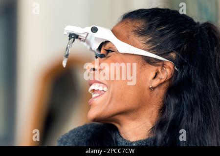 Seitenansicht einer glücklichen schwarzen Kosmetikerin in Vergrößerungsbrille für Mikroblading im Schönheitssalon vor verschwommenem Hintergrund Stockfoto