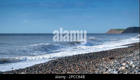 Wellen schlagen auf einen steinigen Strand vor Bootle in Cumbria an der Küste der Irischen See. Cumbria, Großbritannien.
