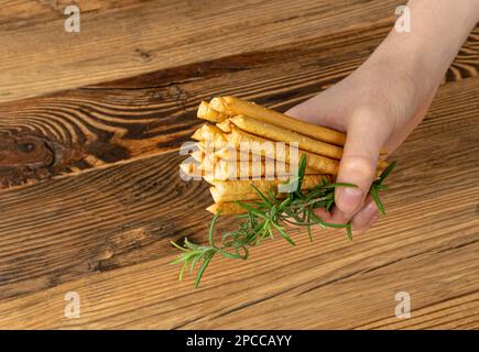 Brotsticks in der Hand, gesalzener Brotstift, Crispy Grissini, trockene hausgemachte Brezeln, Brotstift auf rustikalem Holzhintergrund Stockfoto