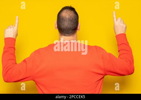 Lateinamerikanischer Mann in rotem Sweatshirt, der mit dem Rücken zur Kamera zeigt, isoliert auf gelbem Hintergrund. Stockfoto
