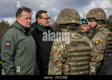 Warschau, Polen. 12. März 2023. Die polnische Verteidigung Mariusz Błaszczak, die Linke und der polnische Premierminister Mateusz Morawiecki stehen während der Veranstaltung „Train with NATO“ am 12. März 2023 in Warschau (Polen) im Mittelpunkt rumänischer Soldaten, die den Sky Guardians, der NATO EFP Battle Group Polens, zugeteilt sind, und sprechen mit ihnen. Kredit: Sergeant Lianne Hirano/U.S. Army/Alamy Live News Stockfoto