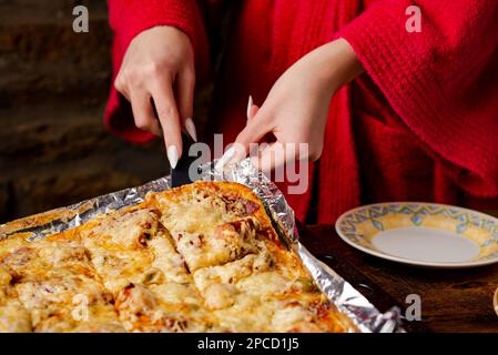 Ein unbekanntes Mädchen nimmt ein Stück hausgemachte Pizza. Die Hand einer Frau mit langen Nägeln hält den Küchenspachtel. Stockfoto