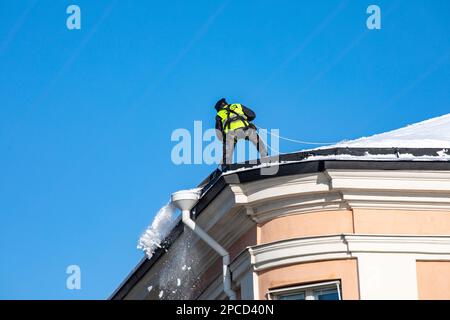 Mann, der an sonnigen Wintertagen im Stadtteil Kruunhaka in Helsinki, Finnland, Schnee von einem Dach schaufelt Stockfoto