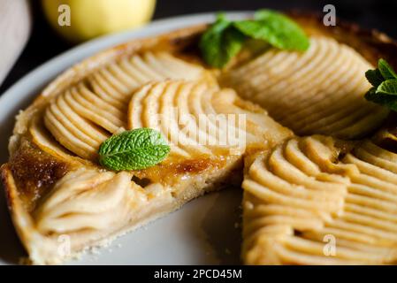 Apfelkuchen aus der Nähe mit Minzblättern. Offener Kuchen mit dünn geschnittenen Äpfeln in Zuckersirup. Stockfoto