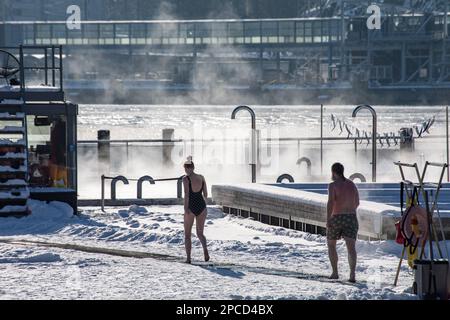 An einem sonnigen Wintertag in Helsinki, Finnland, gehen Leute nach der Sauna auf die Schwimmbadterrasse des Allas Sea Pool Stockfoto