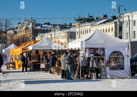 Touristen, die an einem sonnigen Wintertag auf dem Marktplatz in Helsinki, Finnland, Souvenirstände durchstöbern Stockfoto