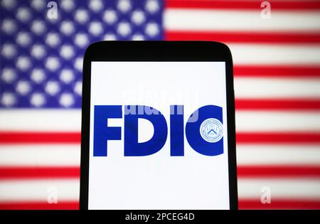 In dieser Fotoabbildung ist das FDIC-Logo (Federal Deposit Insurance Corporation) auf einem Smartphone und die US-Flagge im Hintergrund zu sehen. Stockfoto