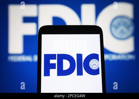 In dieser Abbildung ist das FDIC-Logo (Federal Deposit Insurance Corporation) auf einem Smartphone und im Hintergrund zu sehen. Stockfoto