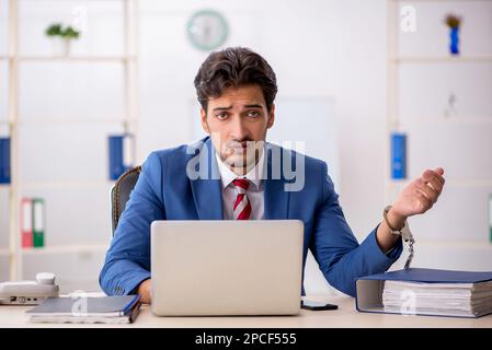 Im Büro sitzender junger Geschäftsmann in Handschellen Stockfoto