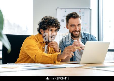 Brainstorming. Aufgeregte, zufriedene männliche Kollegen, die in einem kreativen Büro zusammenarbeiten, ein Notebook verwenden, ein neues Projekt besprechen, Termine planen, potenzielle Kunden und eine Beförderungsstrategie planen, lächeln Stockfoto
