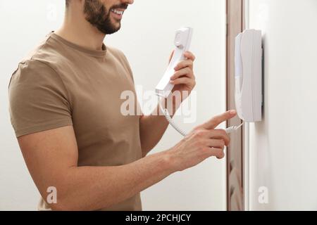 Mann, der den Knopf an der Gegensprechanlage drinnen drückt, schließen Stockfoto