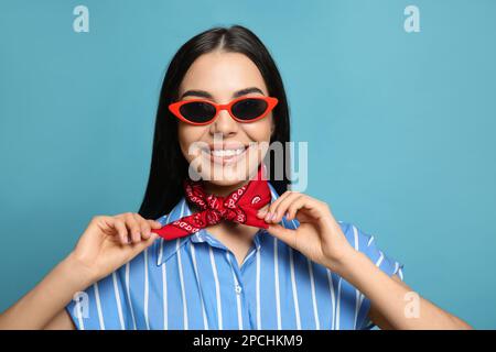 Modische junge Frau in stilvollem Outfit mit Bandana auf hellblauem Hintergrund Stockfoto