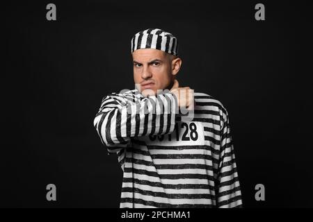 Gefangener in gestreifter Uniform, mit Kehldurchschnitt-Geste auf schwarzem Hintergrund Stockfoto